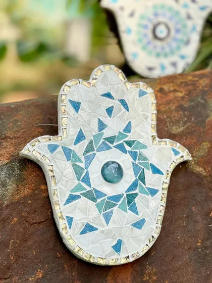 A handmade Hamsa amulet, crafted from blue and white mosaic tiles. This ancient symbol of protection is a beautiful way to add color and positive energy to a garden or indoor space.
