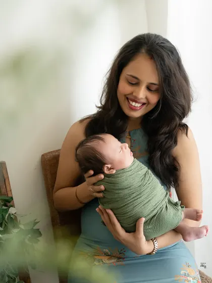A mother's joyful smile as she holds her sleeping baby. The natural light and earthy green tones of the swaddle give this portrait a fresh and organic feel.