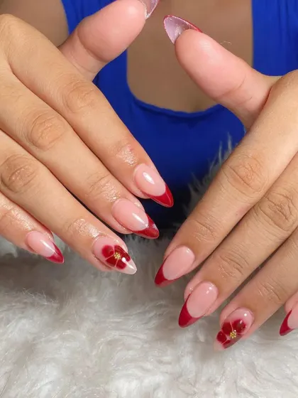 A sharp stiletto set with a deep red French tip and accent nails featuring beautiful, hand-painted red flowers.