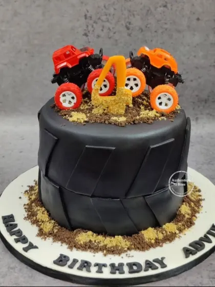 A monster truck cake for a 4th birthday. This cake is designed to look like a giant tire, with two monster trucks on top of edible dirt.