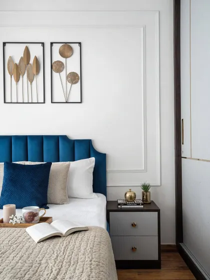 Another angle of the bedroom, showing how the blue upholstered bed and floral metal art piece inside the wall moulding create a captivating and elegant focal point.