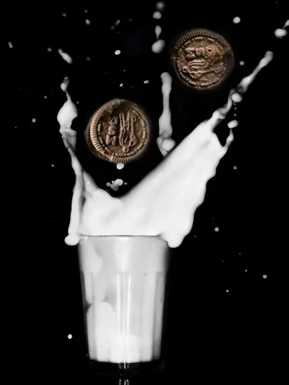 An action shot capturing Oreo cookies splashing into a glass of milk. The high-speed photography freezes the motion, creating a dynamic and fun image that's perfect for a commercial campaign.