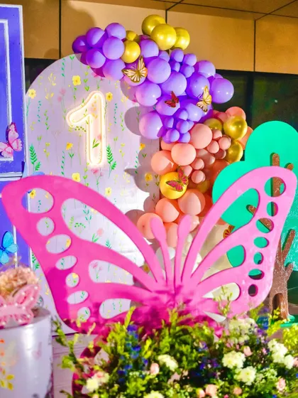 A vibrant pink butterfly prop stands out against a colorful balloon garland. I use a mix of large-scale props and balloon art to create dynamic and eye-catching backdrops.