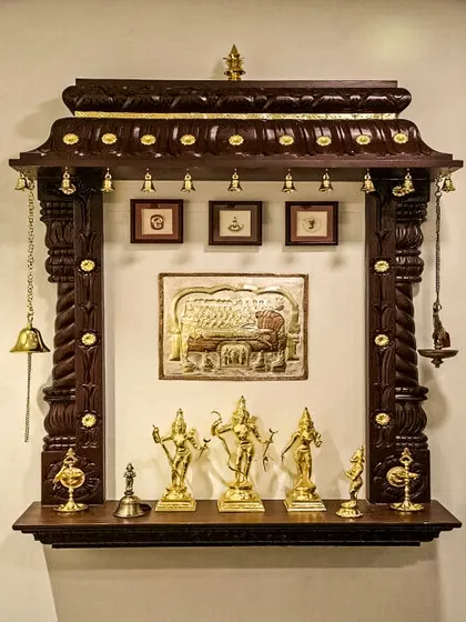 A traditional, wall-mounted wooden pooja mandir with intricate carvings and brass embellishments. This classic design includes a row of small brass bells and a shelf for idols and pictures.