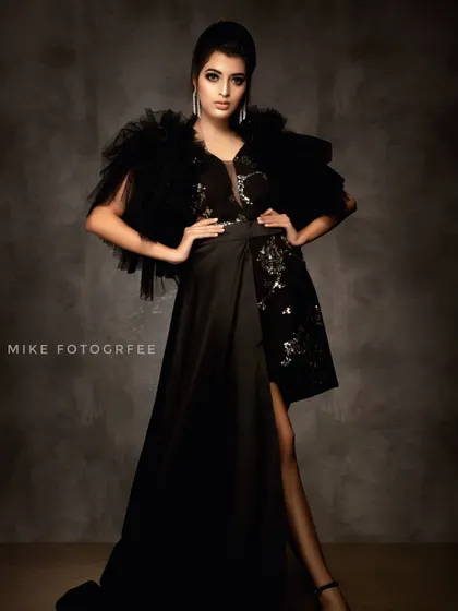 A powerful full-length portrait in a dramatic black gown with tulle shoulders. The strong, confident pose and moody studio backdrop create a look of pure high fashion.