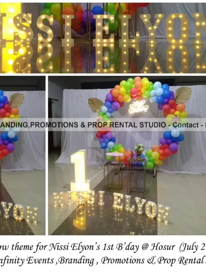 A simple and elegant rainbow theme for a first birthday in Hosur. This outstation event features a transparent circular backdrop with a full rainbow balloon ring, a light-up number "1," and marquee letters for a modern and colorful look.
