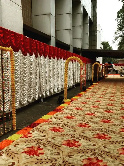 A long and traditional walkway for a wedding at Ramada Navi Mumbai. The path is lined with drapes and marigold flower arrangements, creating a classic and festive entrance.