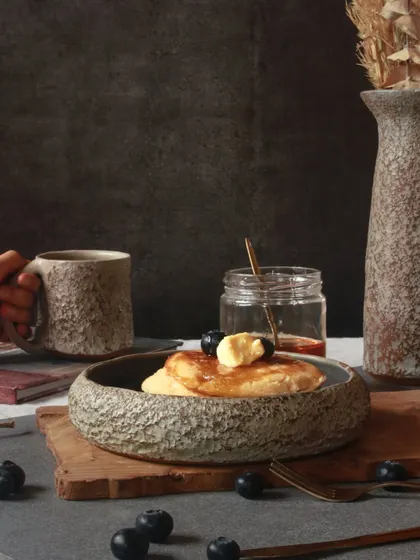A breakfast scene featuring pieces from 'The Rock' Collection. The textured mug and bowl are perfect for everyday rituals, adding a touch of bold, unpolished beauty.