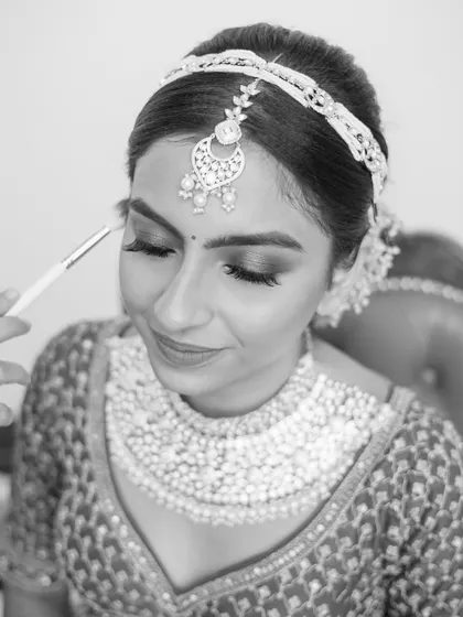 A black and white shot of a bride getting her makeup done, a moment of calm before the ceremony.