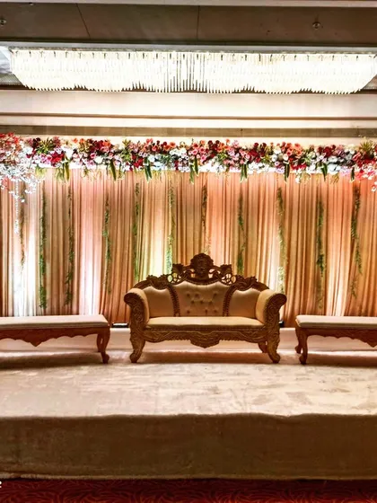 This reception stage combines a classic floral arch of red and white flowers with elegant traditional furniture. The warm lighting and draped background create a timeless and inviting atmosphere for the couple.