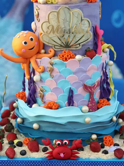 A magnificent multi-tiered mermaid cake. This creation is covered in fondant scales, waves, and coral, and features several characters like an octopus and a crab.