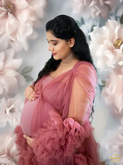 A close-up portrait against a floral backdrop. The soft pink tulle gown and the mother's gentle expression create a very romantic and delicate image.