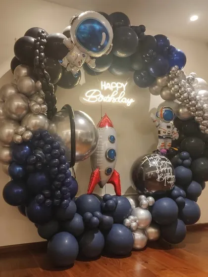 To infinity and beyond! We created this spectacular spaceship-themed organic balloon ring for a young astronaut's birthday. The design features a full circle of balloons in deep space blues, blacks, and metallic silvers, complete with astronaut and rocket ship foils, and a glowing "Happy Birthday" neon sign at the center.
