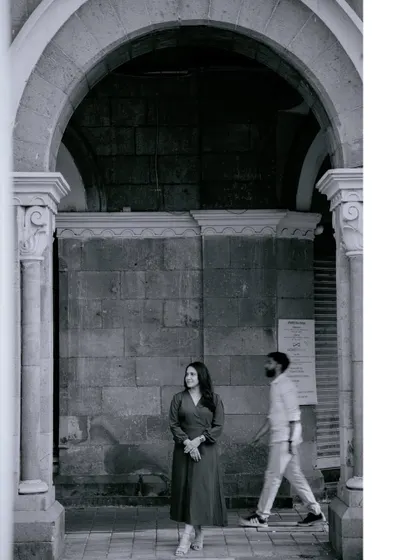 An artistic black and white shot of the bride-to-be standing under a stone archway, while her partner walks past in the background. This creative composition tells a story of moments in time.