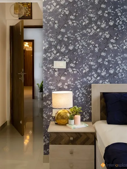 A view from the bed towards the door, highlighting the floral wallpaper and the stylish bedside table with a lit lamp, creating a cozy evening ambiance.