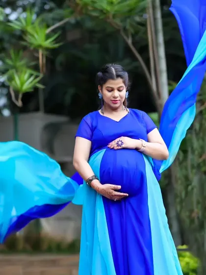 An elegant shot of a woman cradling her baby bump, with the fabric of her blue trail gown flowing around her.