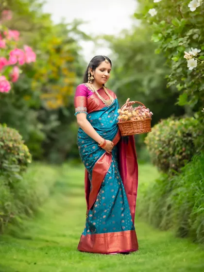 A beautiful outdoor portrait of a mom-to-be in a traditional blue and pink silk saree, walking through a lush garden.