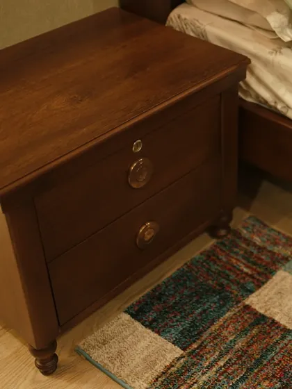 Detail matters. This close-up shows a custom-made teak wood bedside table with classic turned legs and elegant hardware, placed next to a colorful rug.