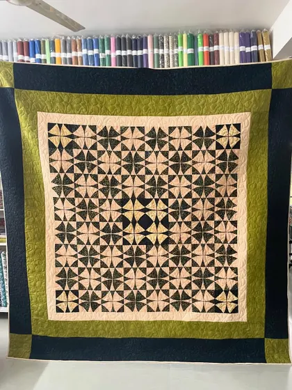 A "Wheel of Mystery" quilt with a complex, circular pattern created from simple blocks. The olive and black color scheme is sophisticated.