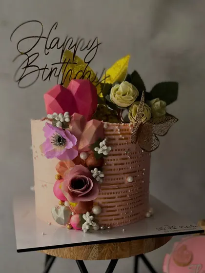 I call this my "love garden" cake. It features a textured buttercream base and is lavishly decorated with sugar flowers, geometric chocolate hearts, and a delicate butterfly.