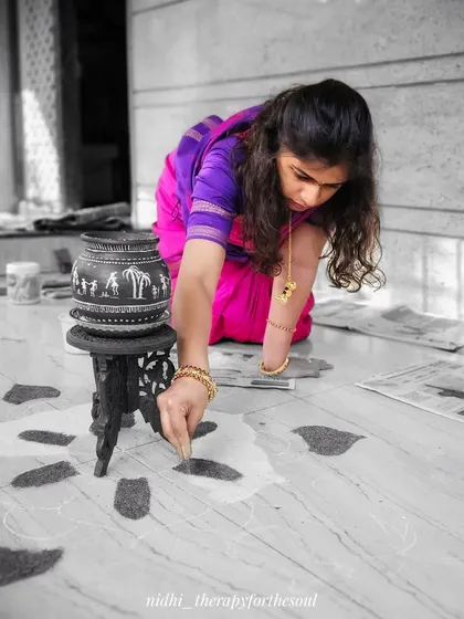 A moment of focus while creating the rangoli. The pot on the stool is one I painted with a Warli art design, ready for the festival.