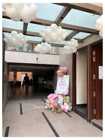The entrance to a high tea party, with cloud-like balloon clusters on the ceiling and a themed welcome sign.