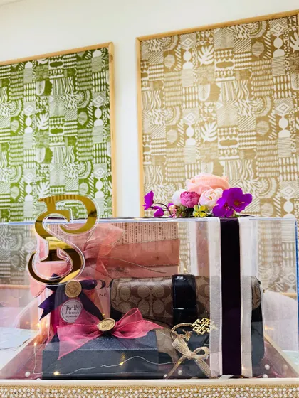 This wide shot shows another version of our acrylic trousseau box, filled with luxury accessories like a Coach pouch. The floral arrangement on top adds a soft, feminine touch.