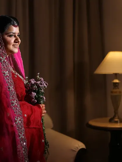 A quiet moment captured as the bride holds a bouquet, with warm indoor lighting creating a cozy atmosphere.