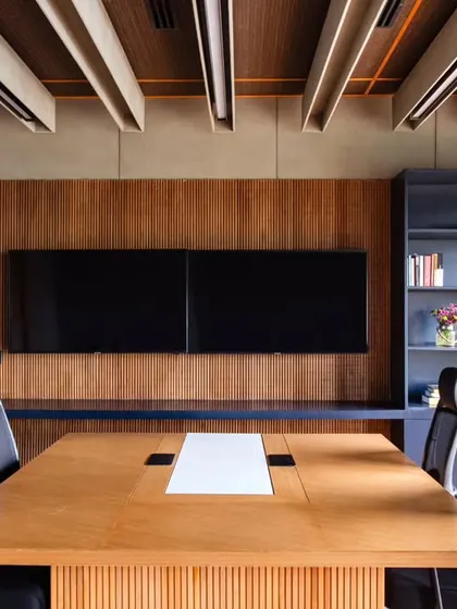 The discussion table area within the Managing Director's cabin at Anthea Pharma. The design features a chatai ceiling treatment and wooden acoustic panels behind the dual screens to ensure excellent sound quality for meetings.