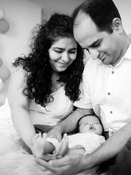 Parents admiring their sleeping newborn's tiny feet. A candid, love-filled moment from a lifestyle family photoshoot at home.