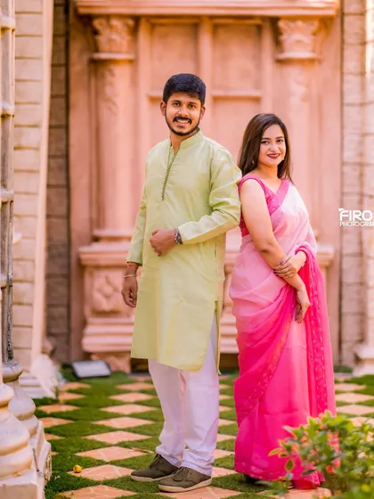 A classic portrait of a couple in matching pink and green traditional outfits. The simple, elegant pose highlights their beautiful attire.