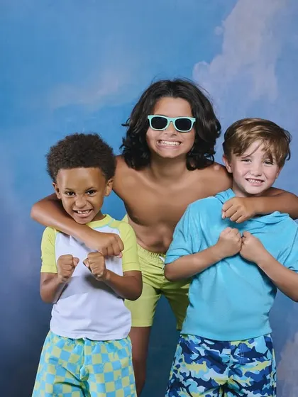 A fun, summery studio shot for a boys' swimwear campaign. The painted cloud backdrop and the boys' energetic poses create a playful and happy vibe.