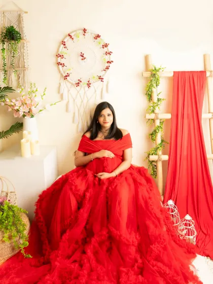 A full-length seated portrait in a stunning red gown. The boho-chic setting provides a beautiful, textured background.