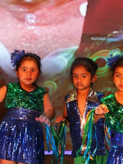 Children in sparkling blue and green costumes perform a dance, their movements synchronized and full of energy.