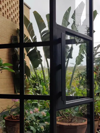 A large glass and metal door at the Sunyata Hotel frames a view of the lush tropical plants outside, blurring the boundary between inside and out.
