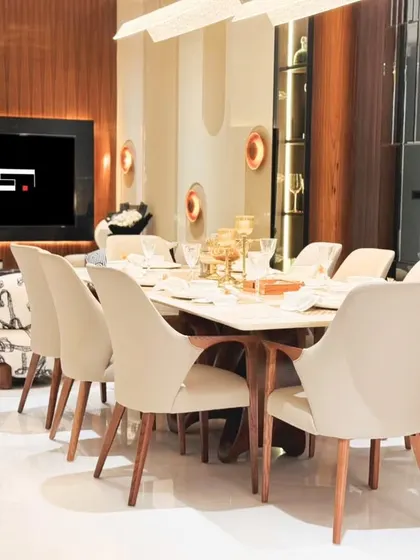 An elegant dining room setup with plush, cream-colored chairs around a large table, perfect for hosting dinner parties. The space is defined by warm lighting and sophisticated decor.