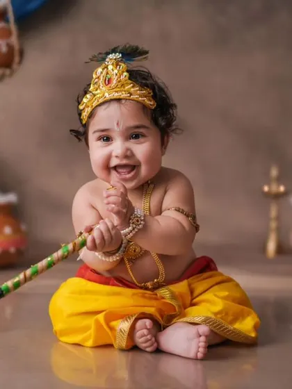 An infectious smile from a baby Krishna, ready for mischief. This studio shot uses a classic setup with hanging butter pots and a vibrant blue background, highlighting the playful nature associated with the deity.