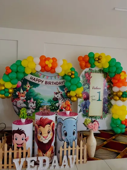 A classic jungle book style setup for a first birthday. It includes a circular backdrop with cartoon animals, character-themed pedestals, and a colorful balloon arch.