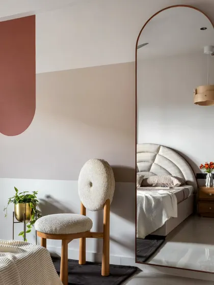 Simple color blocking and a full-length arched mirror create visual play in the guest bedroom without adding clutter. The reflection makes the room feel larger and brighter.