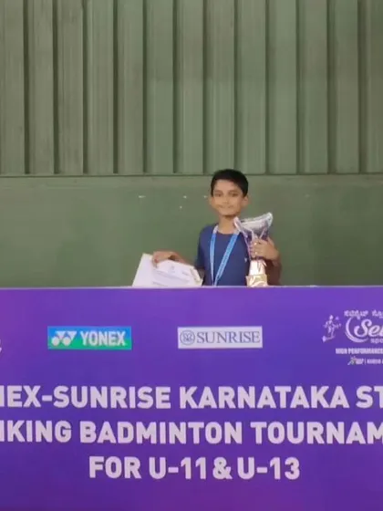 Posing behind the official tournament banner, this image captures the scale of the Yonex-Sunrise Karnataka State Ranking event where our student achieved a podium finish.