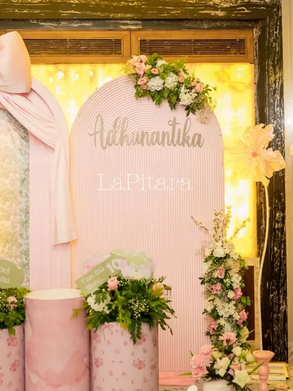 A personalized welcome board for Adhunantika's party, featuring a pink striped arch and delicate floral accents.