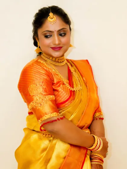 A beautiful portrait of a bride in her silk saree. The makeup enhances her features with a soft glow, defined eyes, and a lip color that complements the warm tones of her outfit.
