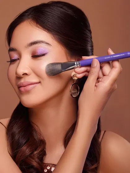 A soft and gentle shot of a powder brush sweeping across the model's cheek. The focus is on the soft application and the beautiful finish it creates on the skin. The model's serene expression conveys a sense of luxury and comfort.
