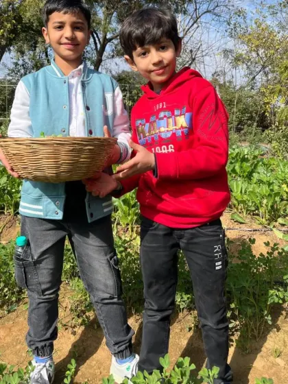 Two young boys proudly holding a basket filled with freshly harvested greens from our organic fields.