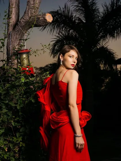 An outdoor evening shot of a dramatic red gown. The flash photography makes the red pop against the darkening sky and lush greenery.