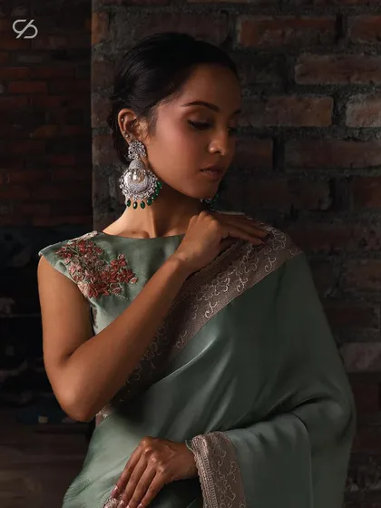 A close-up of the sage green organza saree, paired with a cap-sleeve blouse featuring delicate floral embroidery for a touch of elegance.