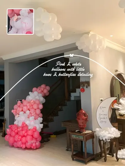Pink and white balloon clouds with little bows and butterfly details floated on the ceiling, creating a dreamy sky for the baby girl's welcome home party.