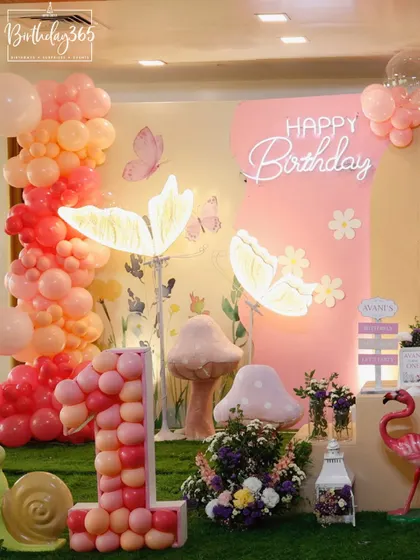 A magical fairy-themed party with glowing butterfly lights, a balloon-filled number "1", and whimsical props like a friendly snail and flamingo.