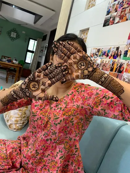 A playful shot of a happy client showing off her engagement mehndi. The design includes the couple's initials inside beautiful mandalas on her palms.