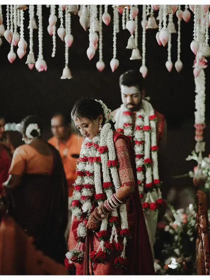 A beautiful portrait of the bride and groom standing together, framed by their long garlands.